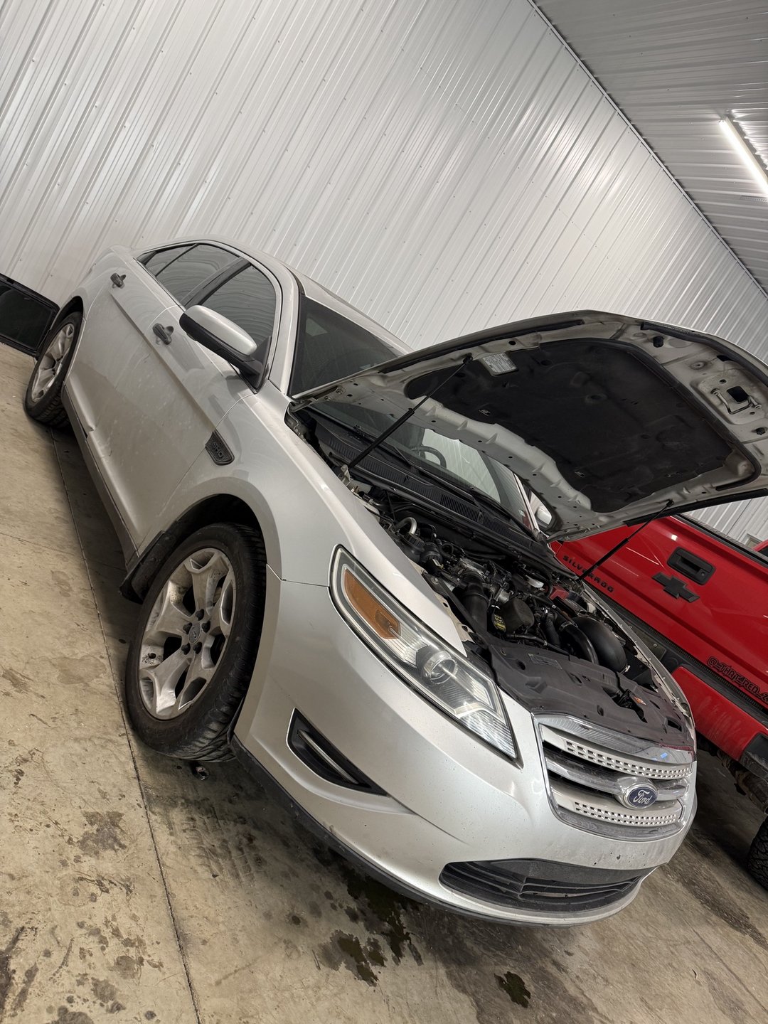 Past shop build — silver 2010 Taurus SHO front three-quarter view with the hood open in the shop