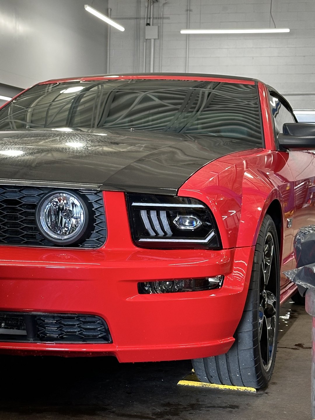 Past shop build — red 2006 Mustang GT convertible front view in the shop, showing its custom headlights and halo fog lights
