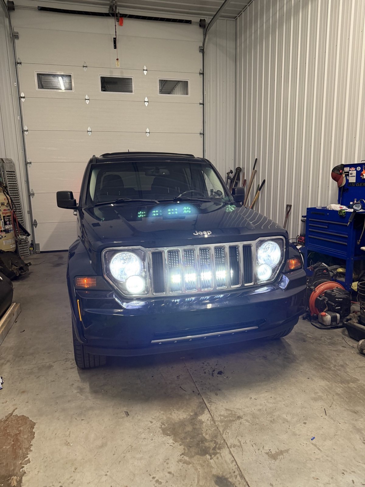 Blue Jeep Liberty in the shop with LED pod lights lit in its grille