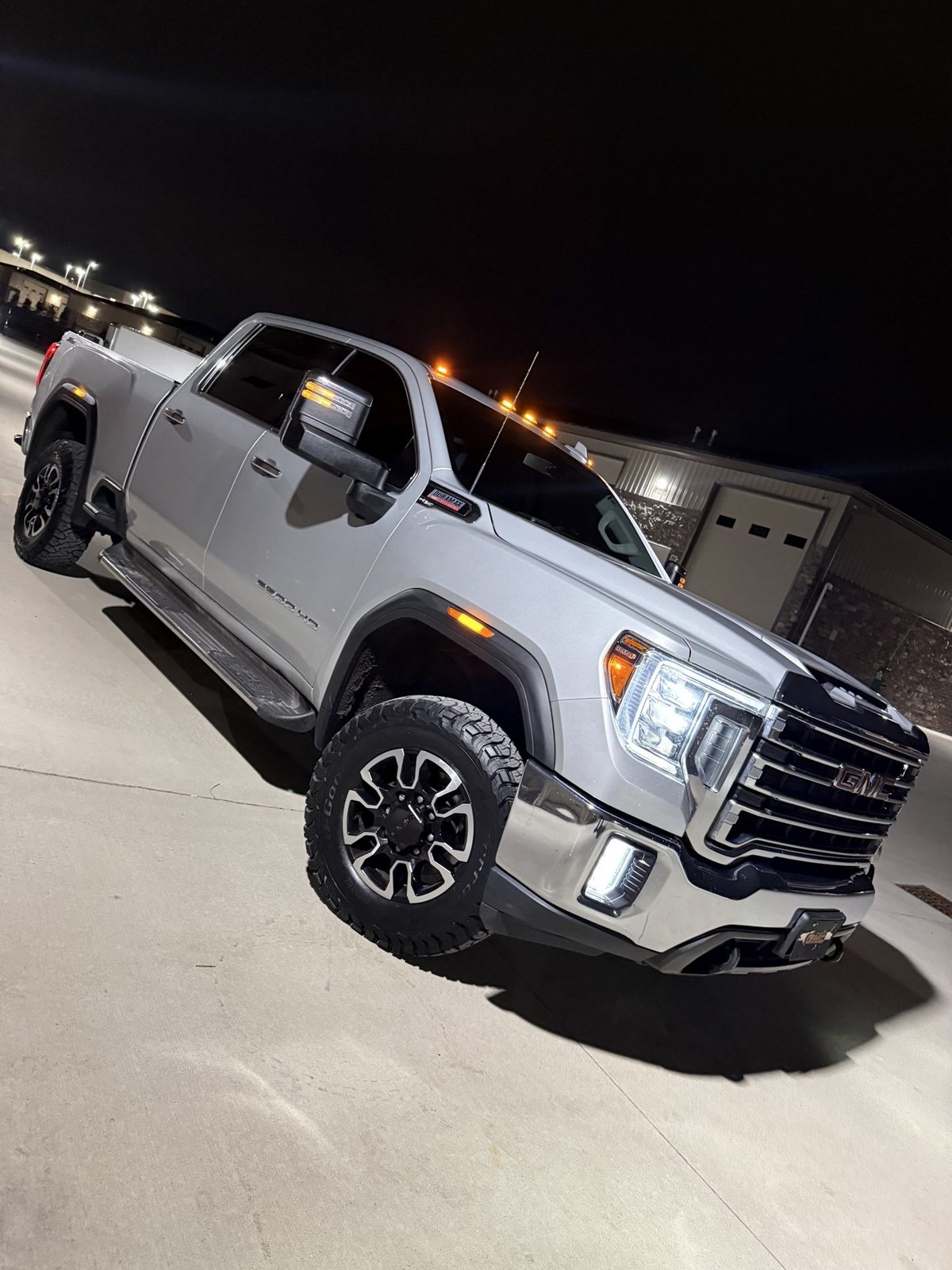 Owner's silver 2020 GMC Sierra 2500HD Duramax side profile at night in front of the storage bays