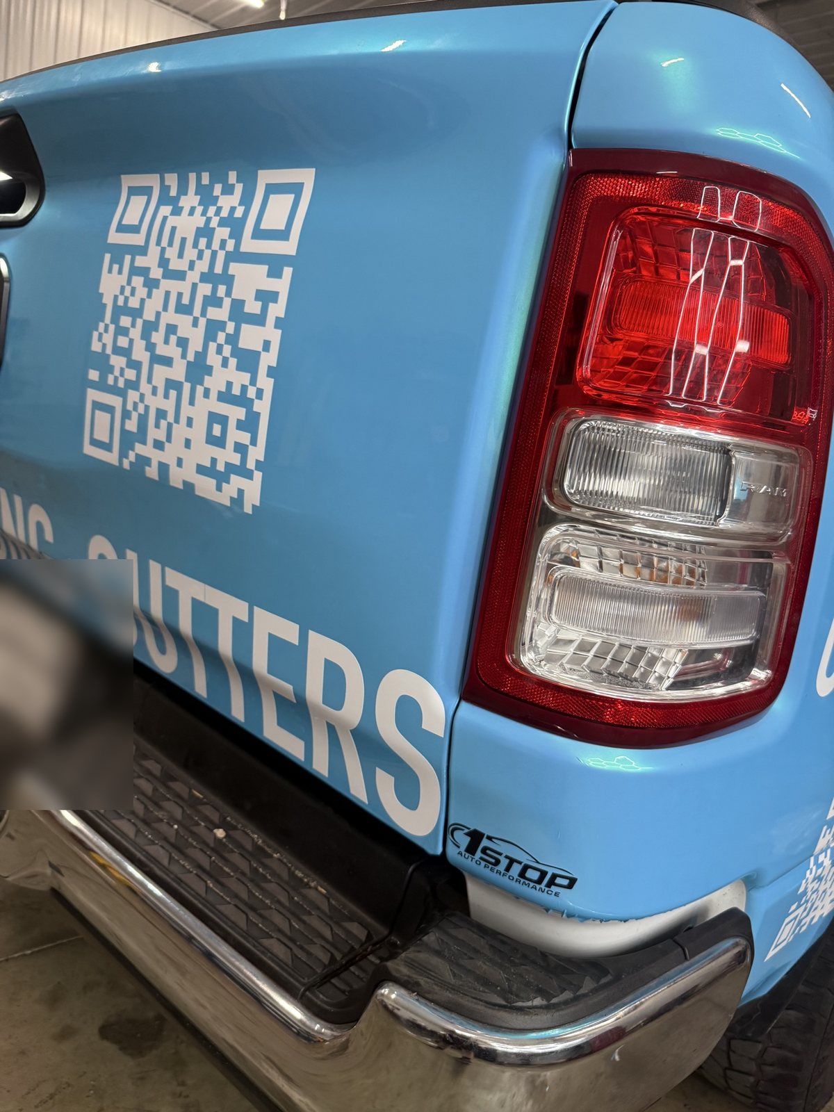 Wrapped Ram tailgate corner detail with QR code and a small 1Stop logo decal