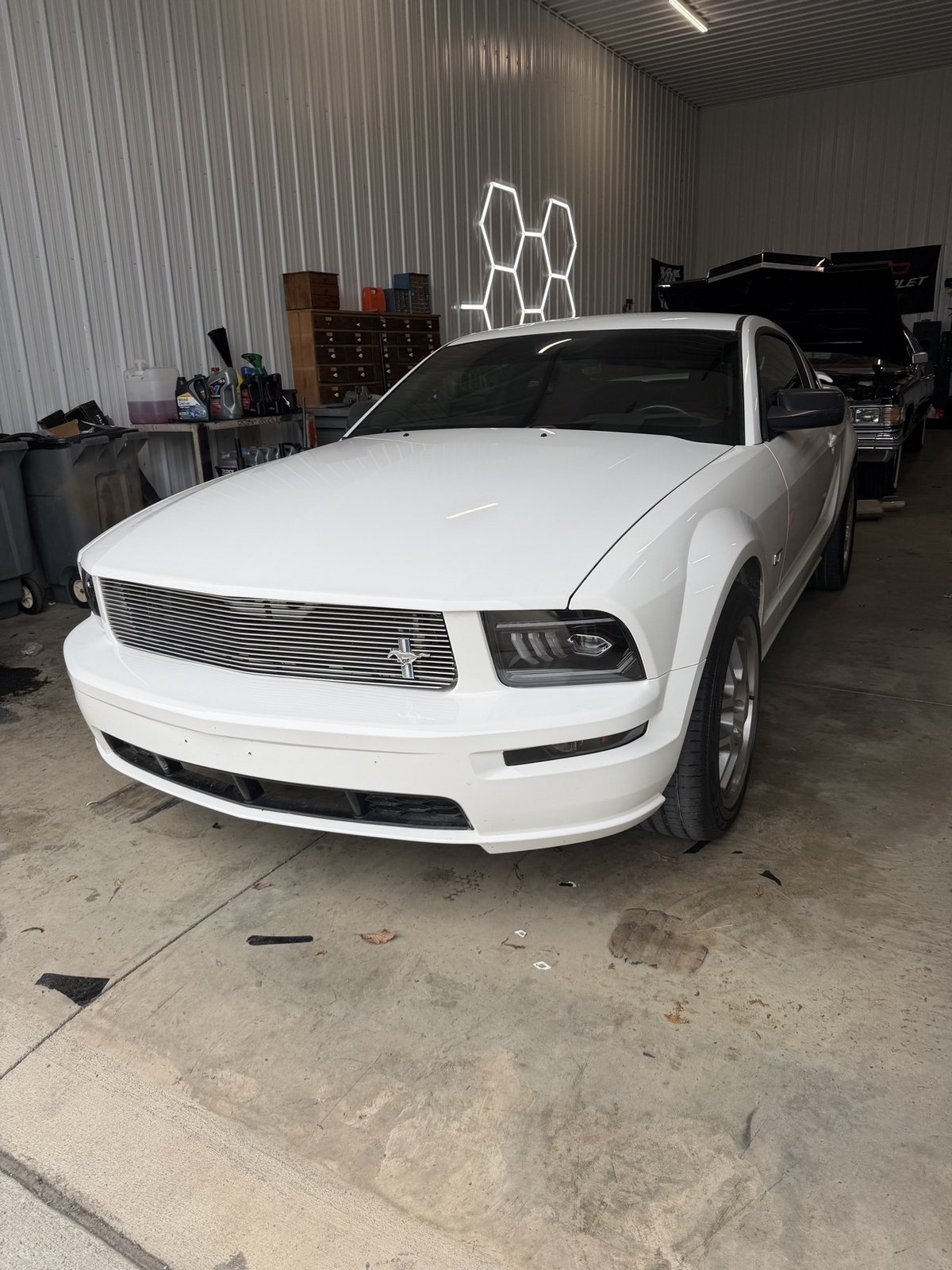 Owner's white 2006 Mustang GT front view in the shop with LED headlights and billet grille