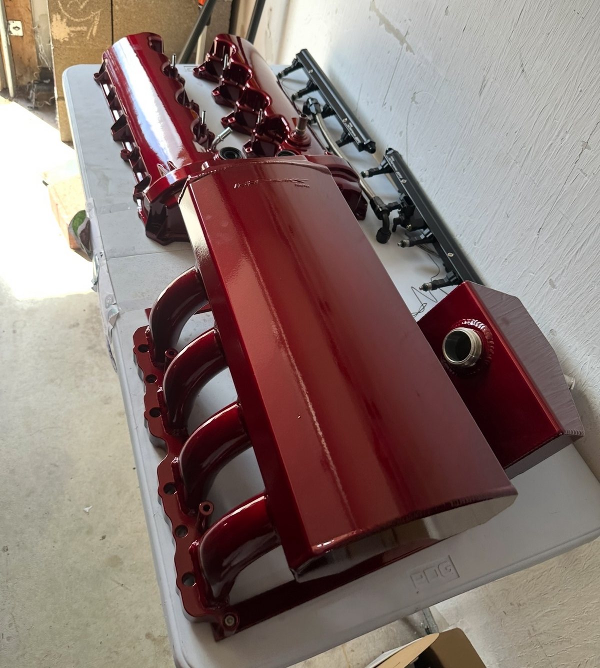 Candy-red powder-coated intake manifold, valve covers and rails laid out on a table