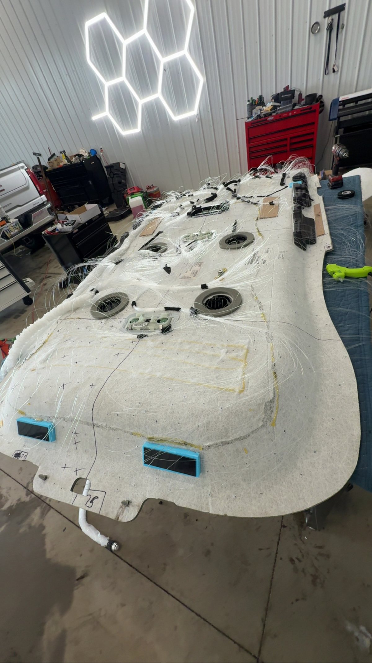 Back side of a headliner board on a table with fiber-optic routing mid-install