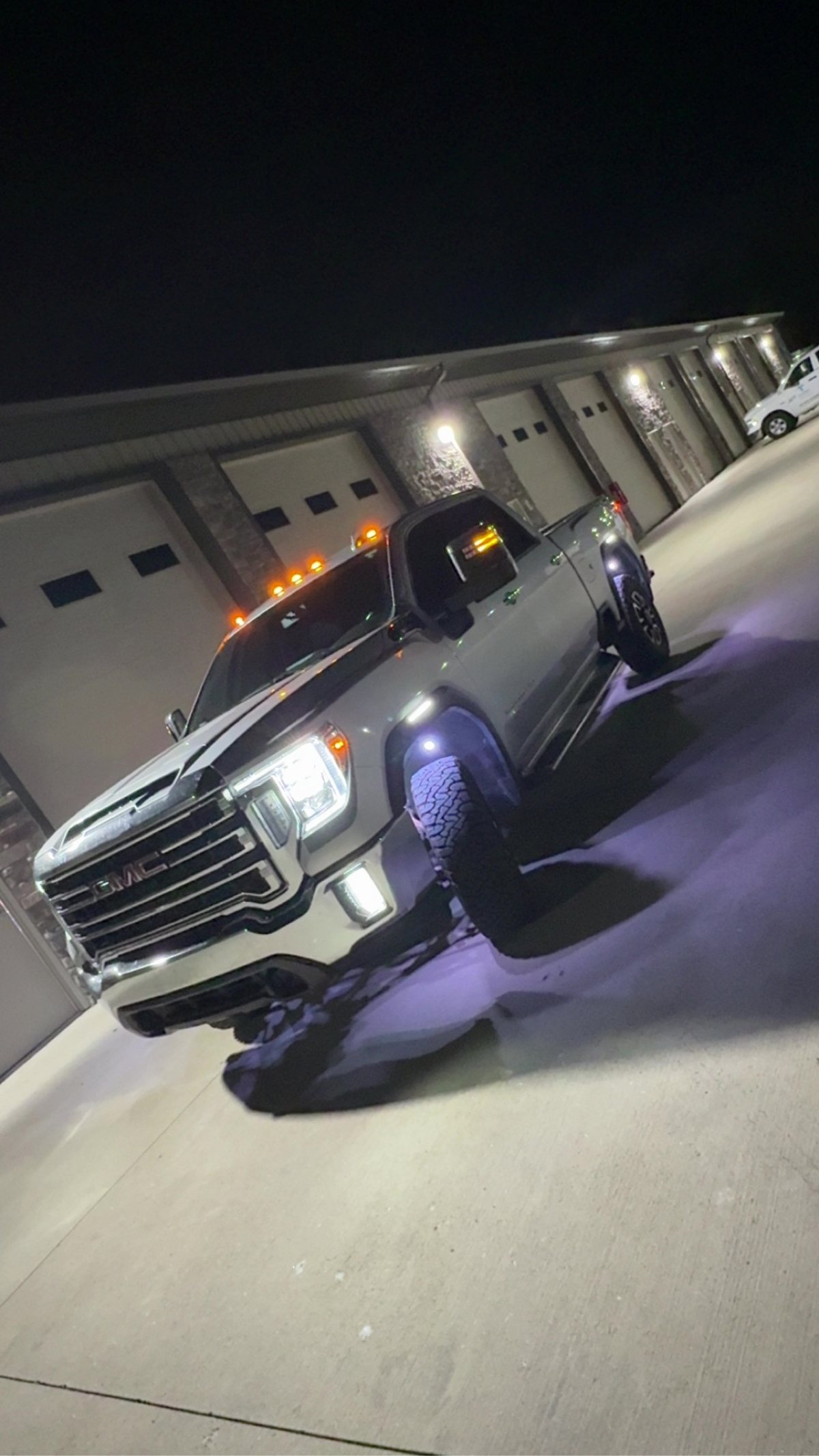 Silver GMC Sierra Duramax at night outside the shop with rock lights, cab markers and LED headlights lit