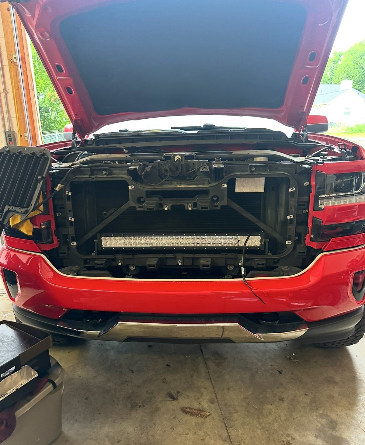 Red Silverado with its grille removed and a light bar mounted behind it during install