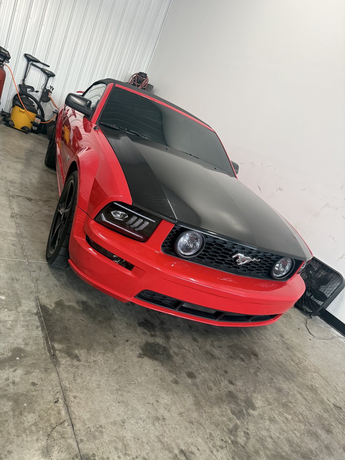 Red Mustang GT convertible in the shop with a black wrapped hood and LED headlights